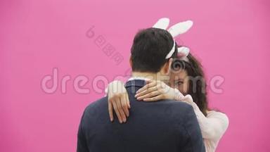 美丽的年轻女孩站在粉红色的背景上。 在这期间，头上有兔子的耳朵。 摆动头